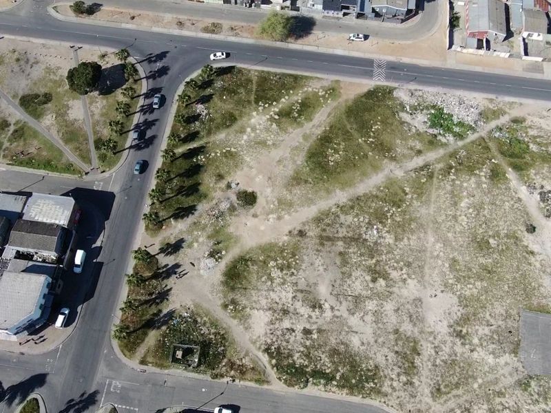 Aerial view of a vacant corner residential plot featuring road access and established palm trees, offering potential for future development.