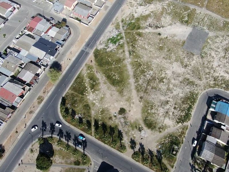 An aerial view of a vacant residential plot situated at a street corner, surrounded by established residential housing and paved road infrastructure.