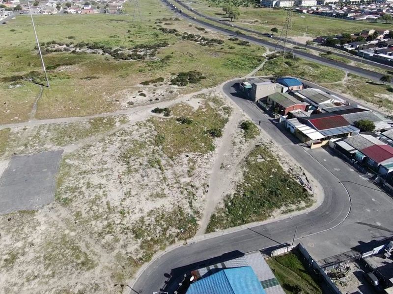 Aerial view of a vacant residential plot situated adjacent to an existing neighborhood and paved road infrastructure.