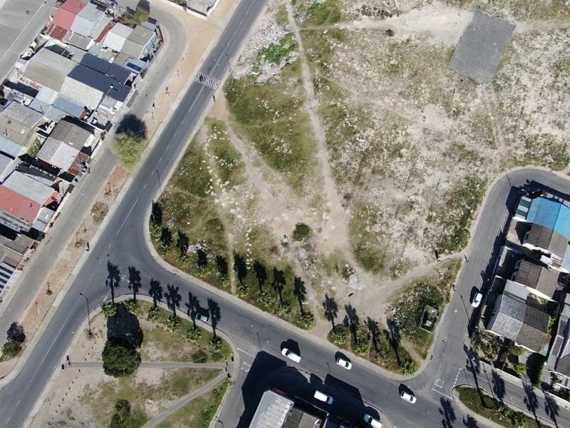 An aerial view of a vacant residential plot situated at a street corner, surrounded by established residential infrastructure.