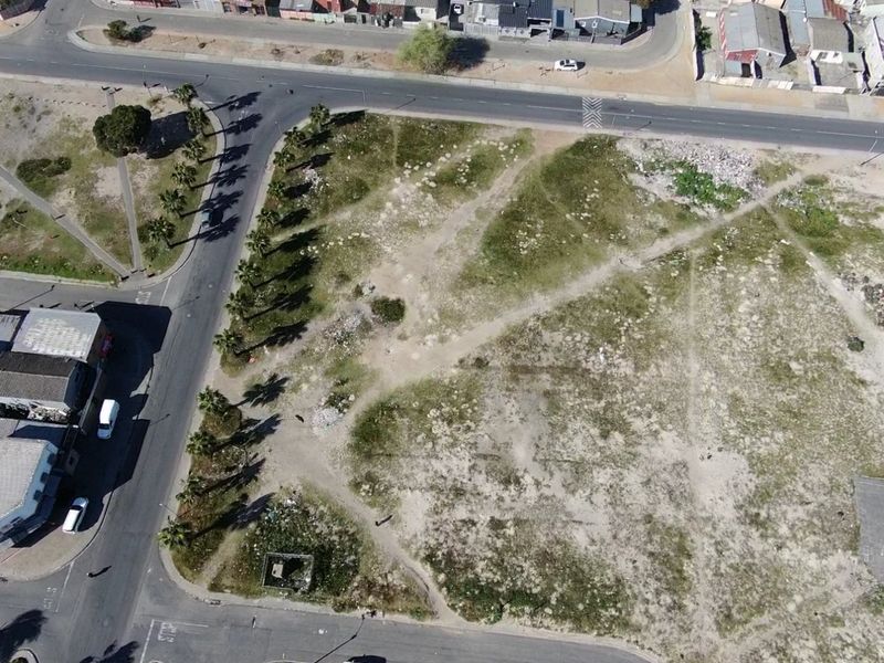 Aerial view of a vacant residential corner plot featuring established palm trees and direct access to surrounding paved roads.