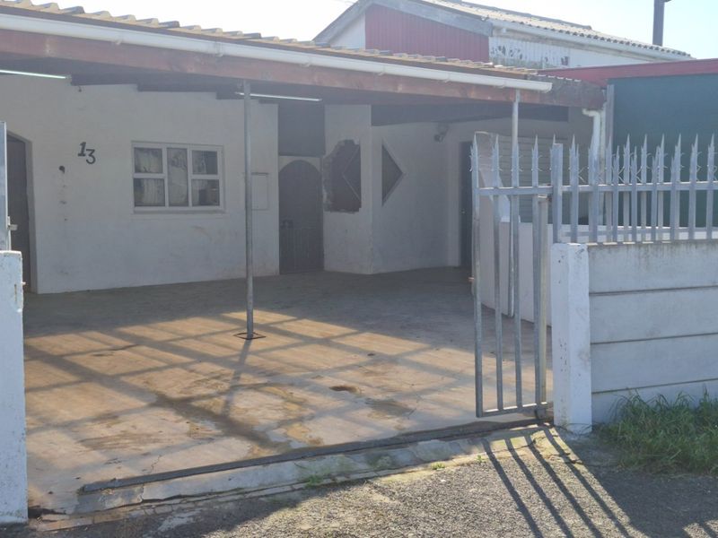 Front exterior view of the property featuring a concrete driveway, covered carport, and secure perimeter wall with metal fencing.