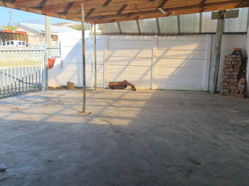 A covered outdoor patio area featuring a timber roof structure, concrete flooring, and a secure metal gate entrance.