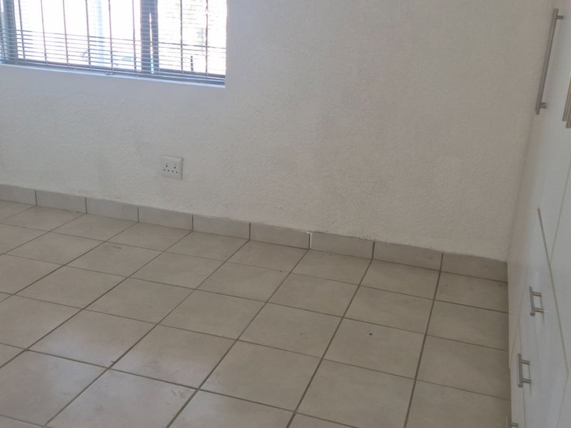 An empty bedroom featuring neutral tiled flooring, built-in white cupboards, and a window fitted with security bars.