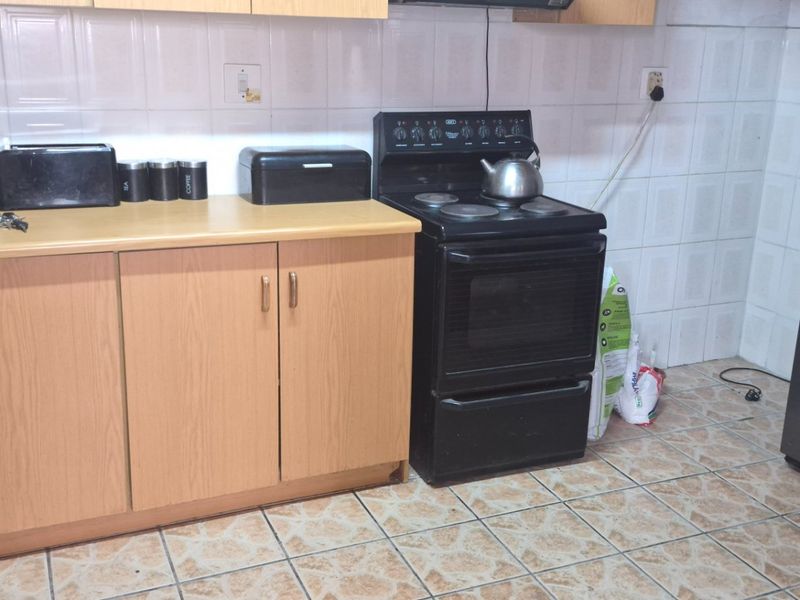 A functional kitchen featuring laminate cabinetry, tiled splashbacks, and a freestanding electric stove, requiring cosmetic updates to modernize the space.