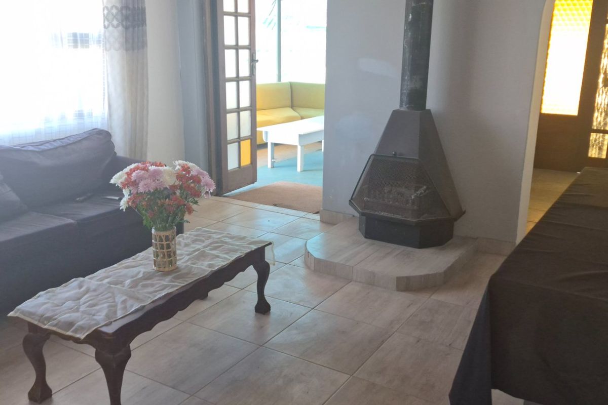 Living room featuring tiled flooring and a central freestanding fireplace, with direct access to an adjoining patio area through a timber-framed glass door.