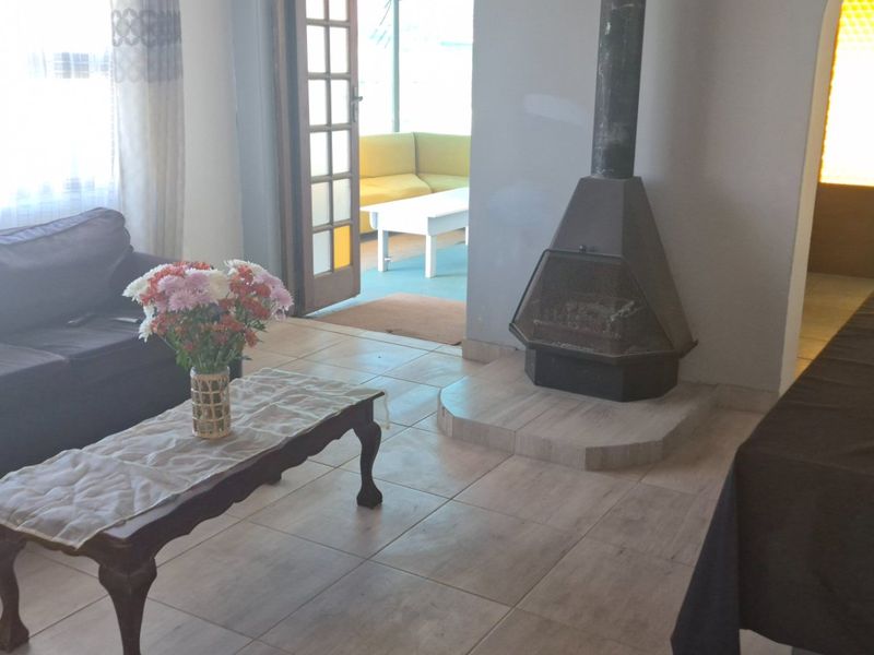 Living room featuring tiled flooring and a central freestanding fireplace, with direct access to an adjoining patio area through a timber-framed glass door.
