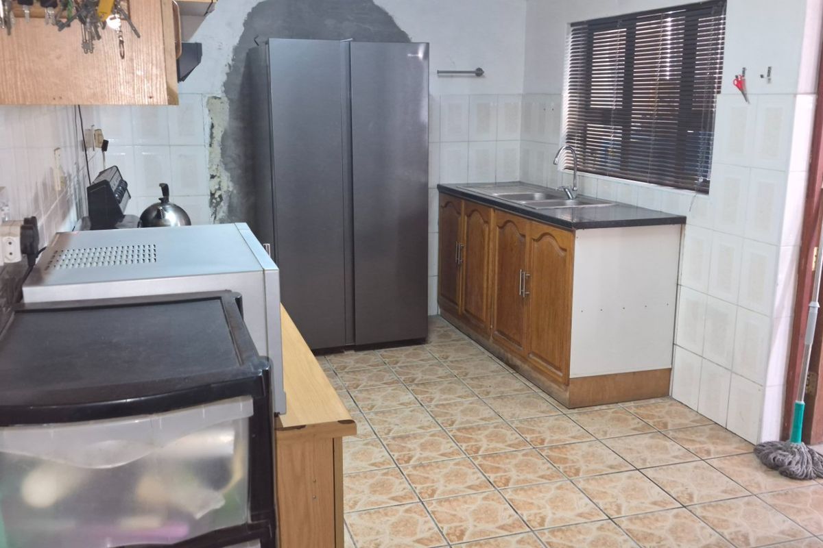 A functional kitchen featuring tiled flooring, wooden cabinetry, a double sink, and a tiled splashback, requiring some cosmetic updates to the wall and finishes.