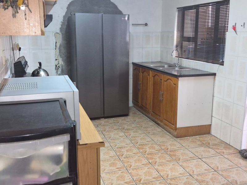 A functional kitchen featuring tiled flooring, wooden cabinetry, a double sink, and a tiled splashback, requiring some cosmetic updates to the wall and finishes.
