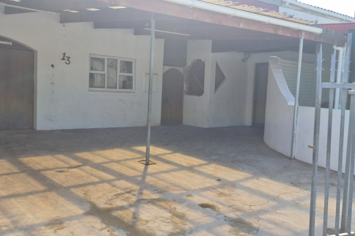 Front exterior view of the property featuring a covered carport, concrete driveway, and security fencing, showing signs of wear and maintenance requirements.