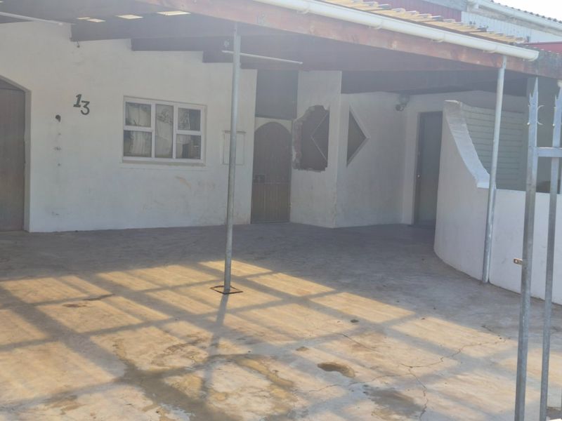 Front exterior view of the property featuring a covered carport, concrete driveway, and security fencing, showing signs of wear and maintenance requirements.