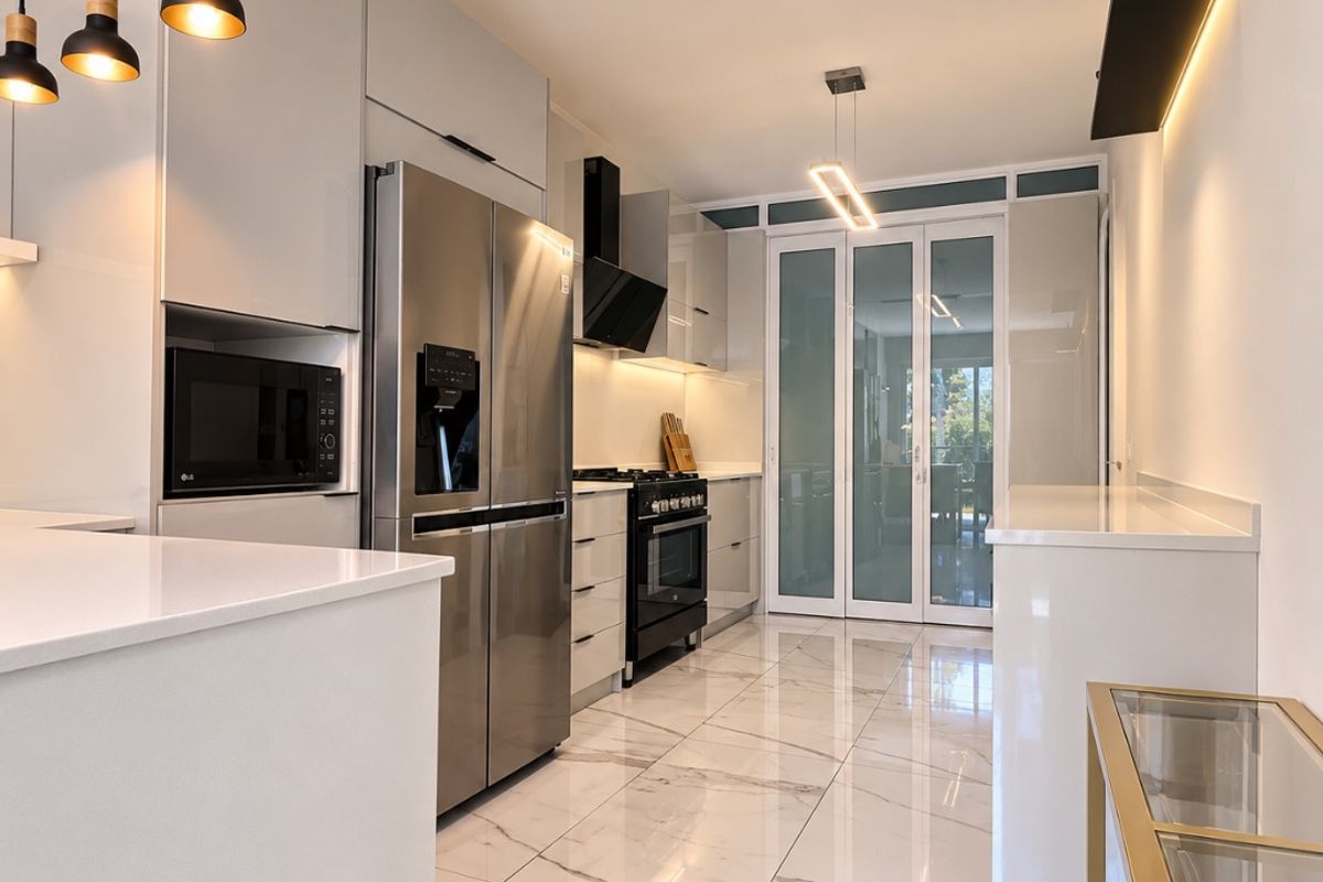 Modern kitchen featuring sleek cabinetry, stone countertops, high-end stainless steel appliances, marble-look flooring, and elegant pendant lighting leading to a glass-paneled entrance.