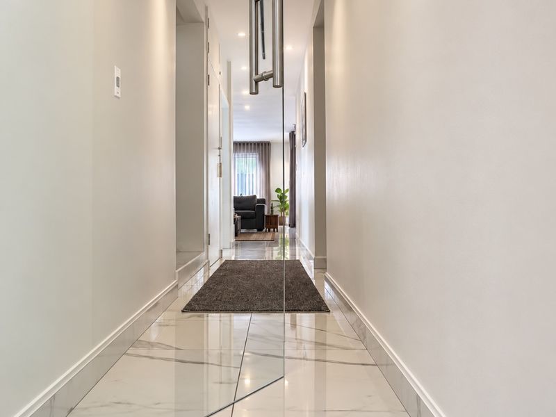 A bright, modern hallway featuring polished marble-look floor tiles, recessed lighting, and a sleek glass pivot door leading into the living area.