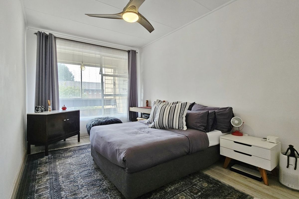 A well-lit bedroom featuring a ceiling fan, large window for natural light, and modern laminate flooring.