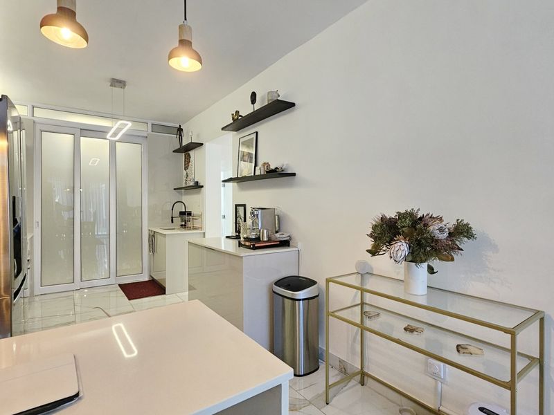 Modern kitchen featuring sleek cabinetry, stone countertops, and contemporary pendant lighting, seamlessly connected to adjacent living spaces through sliding glass doors.