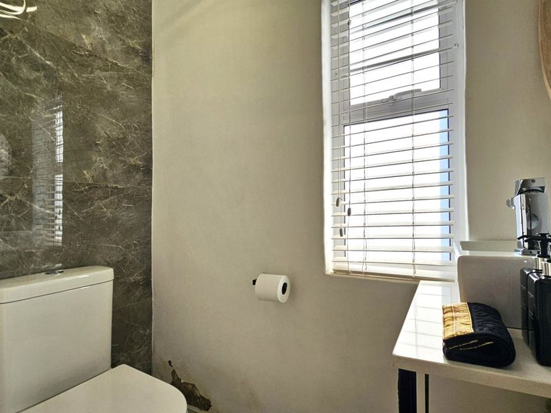 A compact bathroom featuring a modern vanity basin, toilet, and marble-effect feature tiling, with a window providing natural light.