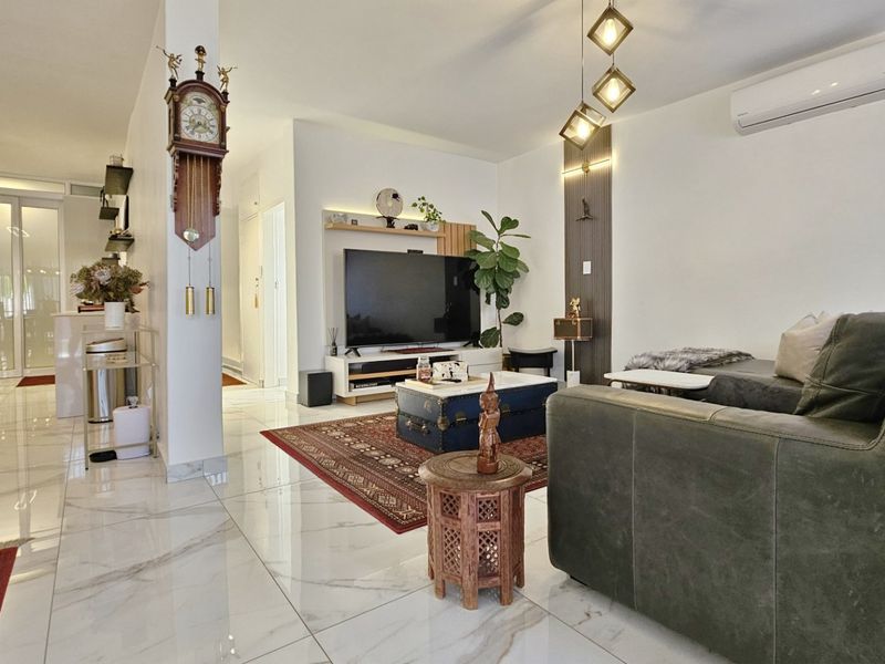A bright and modern living room featuring polished marble-look floor tiles, decorative wall paneling, and a wall-mounted split-system air conditioner.