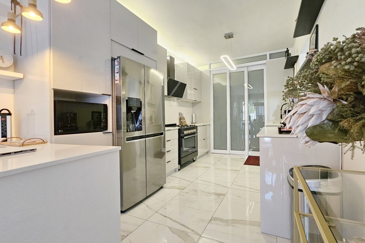 Modern kitchen featuring sleek white cabinetry, stone countertops, high-end built-in appliances, and polished marble-look floor tiles with glass sliding door access.