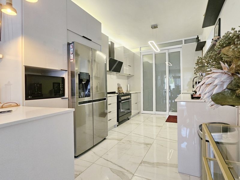 Modern kitchen featuring sleek white cabinetry, stone countertops, high-end built-in appliances, and polished marble-look floor tiles with glass sliding door access.