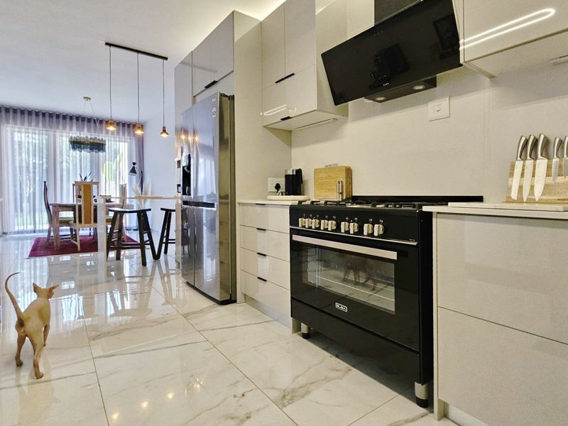 Modern open-plan kitchen featuring high-gloss cabinetry, stone countertops, and a professional-style gas range, flowing seamlessly into the dining area.