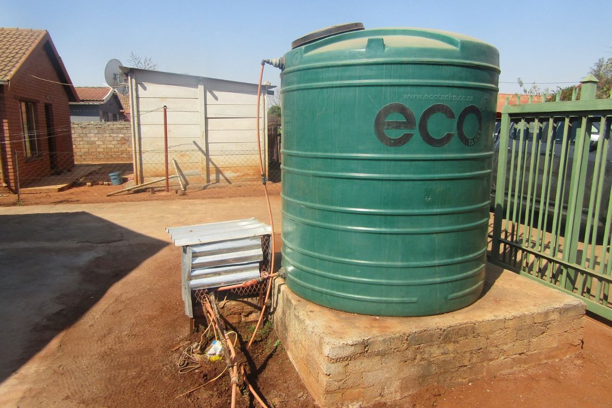 Exterior view of a residential property featuring a green water storage tank mounted on a concrete plinth with associated pump infrastructure.