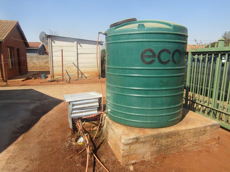 Exterior view of a residential property featuring a green water storage tank mounted on a concrete plinth with associated pump infrastructure.