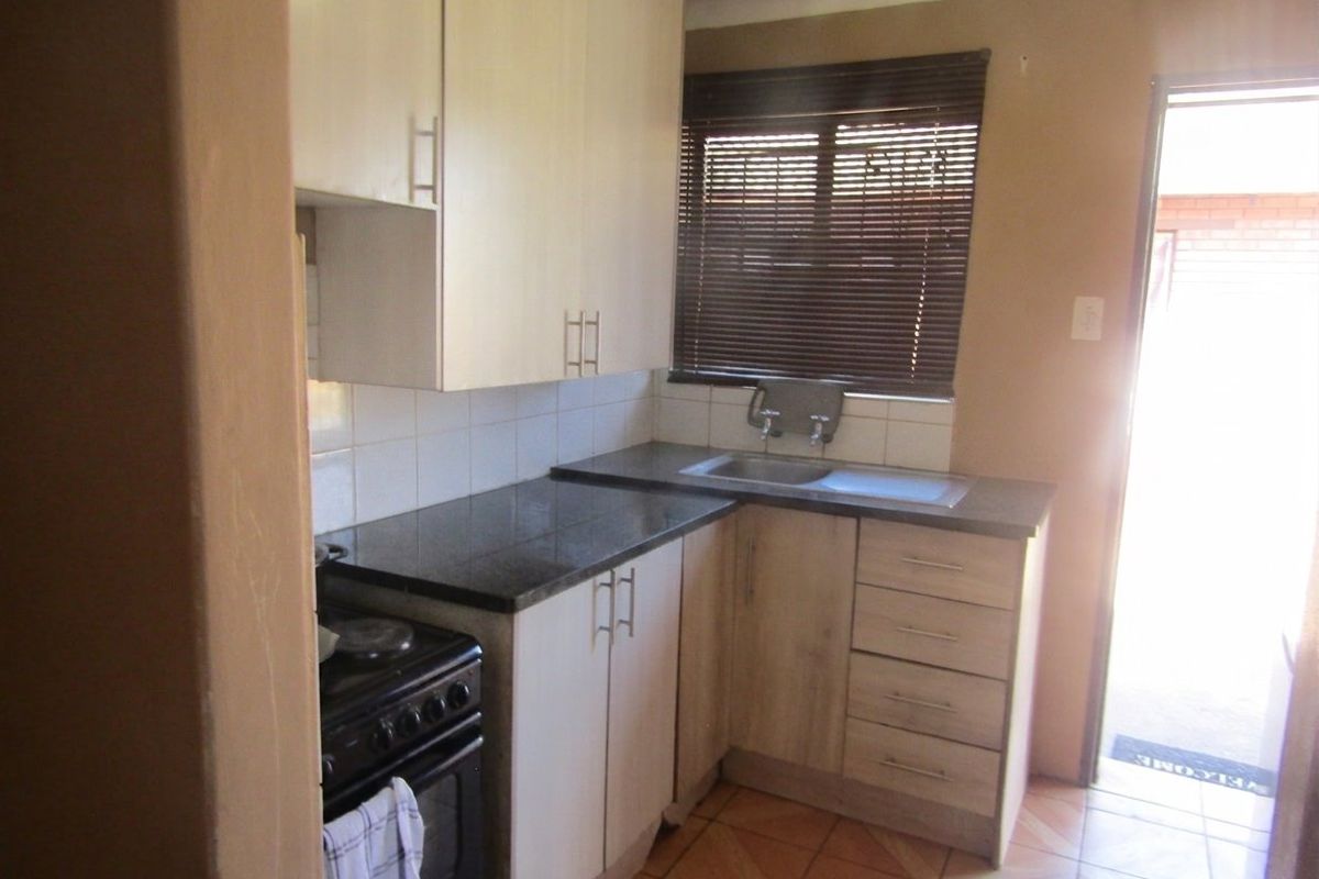 Compact kitchen featuring built-in cabinetry, laminate countertops, stainless steel sink, and tiled flooring with direct access to the exterior.