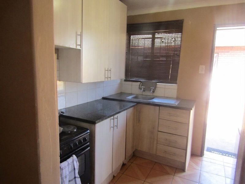 Compact kitchen featuring built-in cabinetry, laminate countertops, stainless steel sink, and tiled flooring with direct access to the exterior.