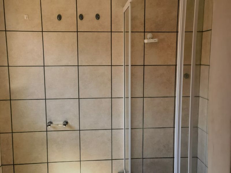 A functional bathroom featuring a shower enclosure, tiled walls and flooring, and a standard toilet. The space is ready for cosmetic updates.
