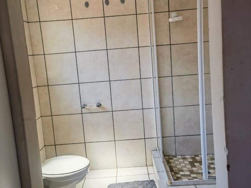 A functional bathroom featuring a shower enclosure, toilet, and neutral wall and floor tiling.