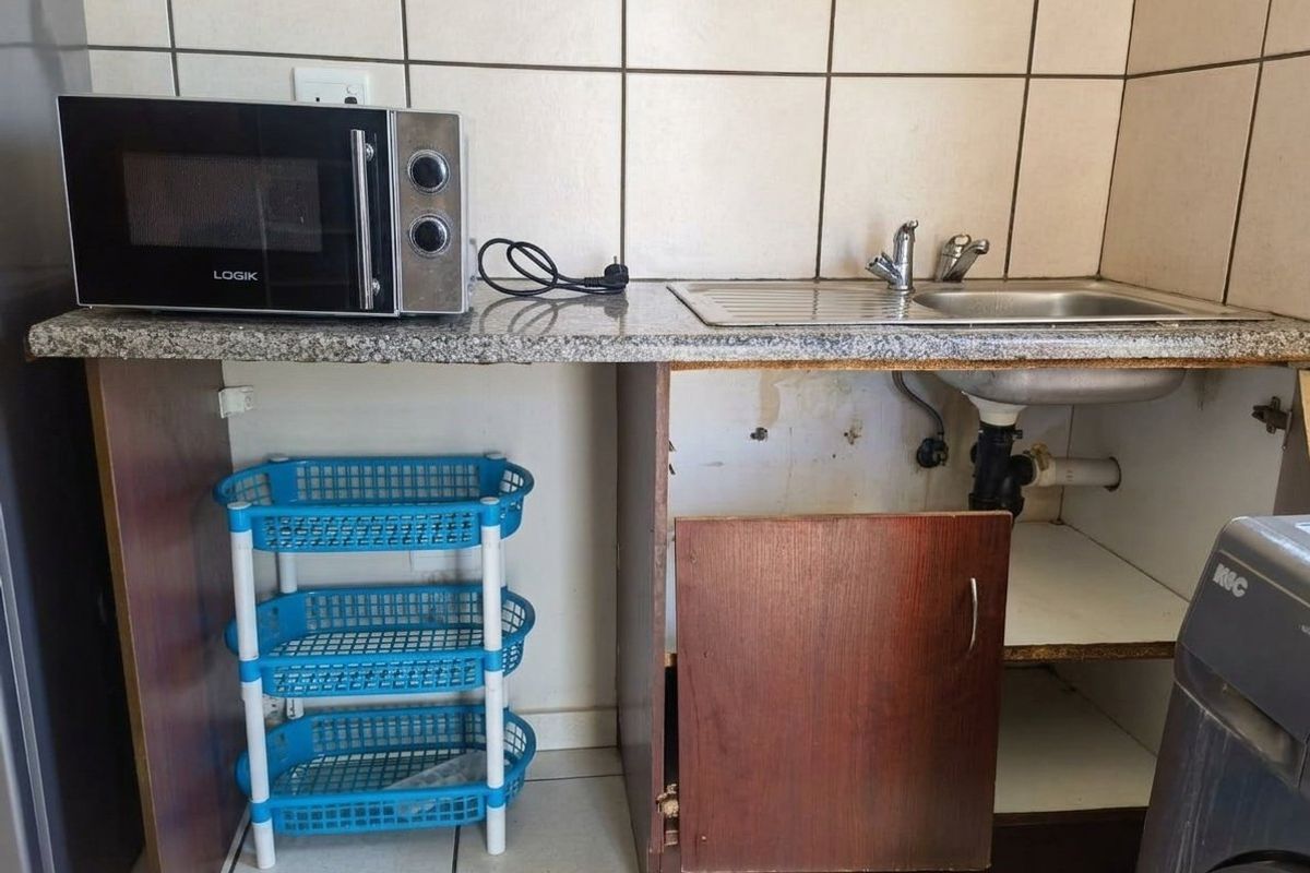 A small kitchen area featuring a granite countertop, stainless steel sink, and tiled backsplash, currently requiring repairs to cabinetry and plumbing.