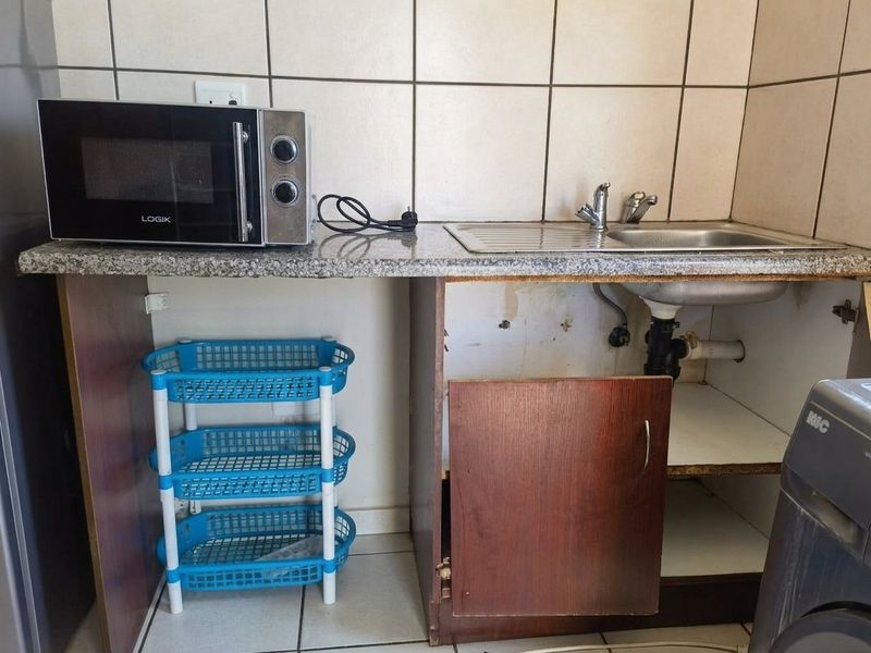 A small kitchen area featuring a granite countertop, stainless steel sink, and tiled backsplash, currently requiring repairs to cabinetry and plumbing.