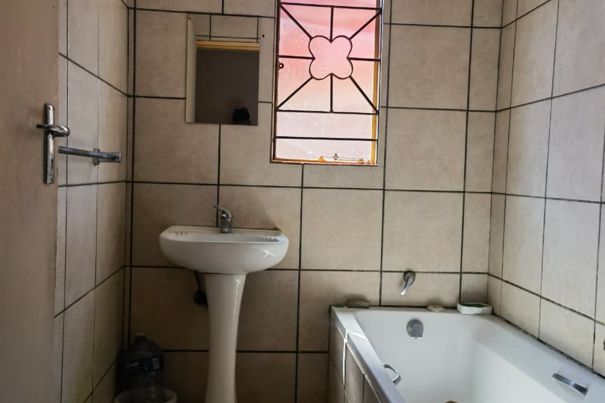 A functional bathroom featuring a pedestal basin, bathtub, and full-height wall tiling, providing a clean and practical space.