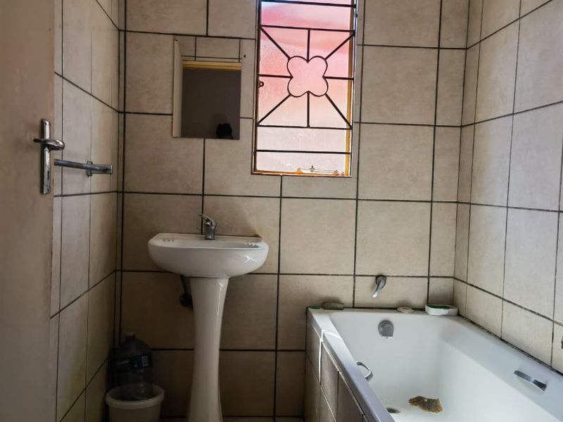 A functional bathroom featuring a pedestal basin, bathtub, and full-height wall tiling, providing a clean and practical space.