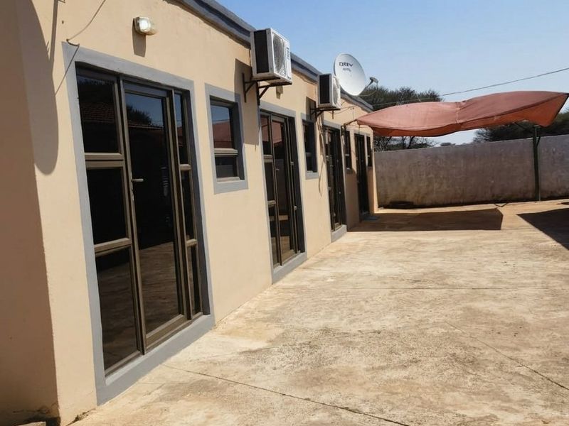 Rear exterior view featuring a concrete patio area, multiple sliding glass door access points, and wall-mounted air conditioning units.