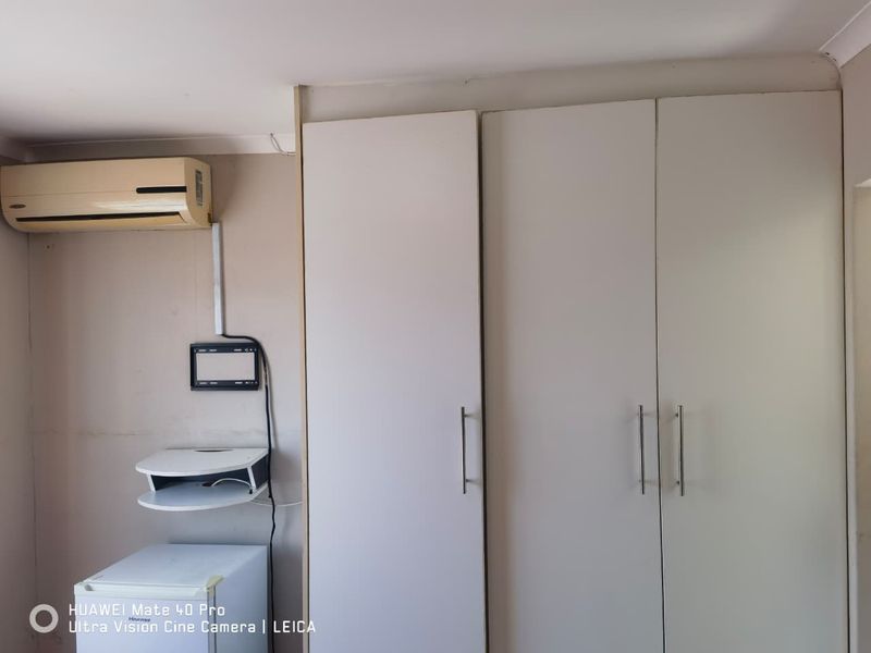 A bedroom interior featuring built-in cupboards and a wall-mounted air conditioning unit, showing signs of wear and requiring cosmetic updates.