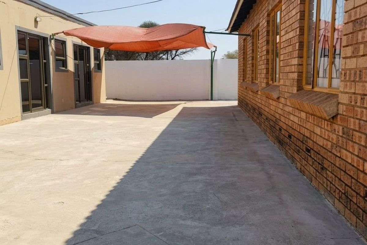 A paved rear courtyard area featuring a brick exterior wall, aluminium window frames, and a shade sail structure.