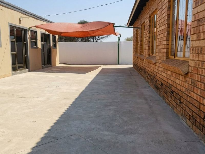 A paved rear courtyard area featuring a brick exterior wall, aluminium window frames, and a shade sail structure.