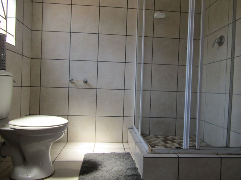 A functional bathroom featuring a tiled shower enclosure and a standard toilet, finished with neutral wall and floor tiles.