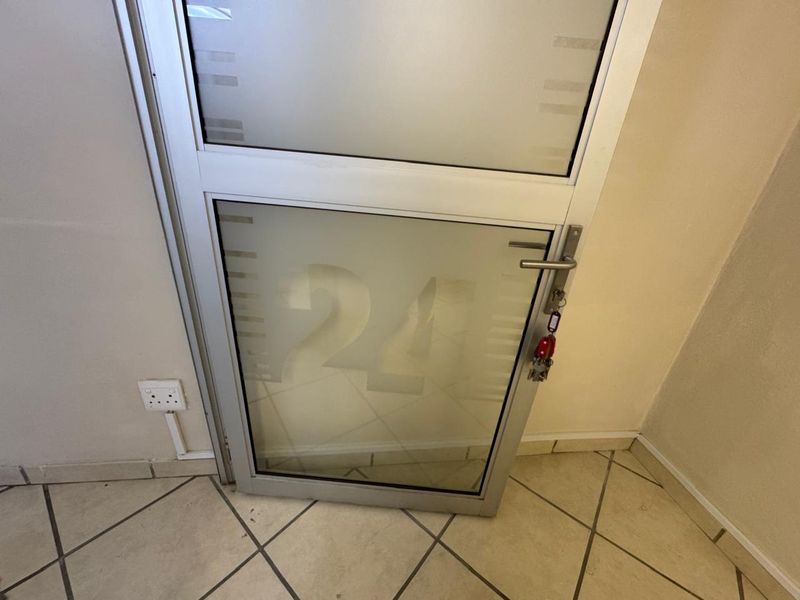 A commercial entry door featuring frosted glass panels with unit number branding, set within an aluminum frame and tiled flooring.