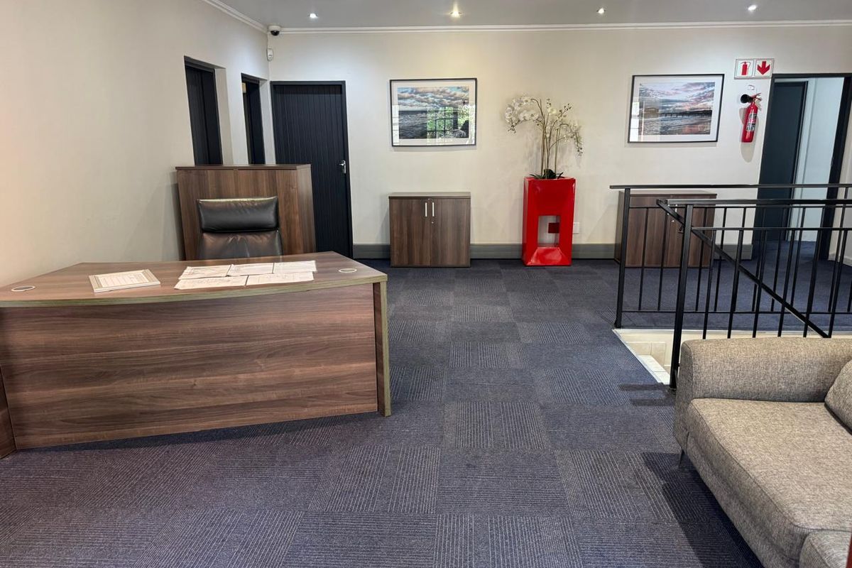 A professional office space featuring carpeted flooring, recessed downlighting, and a metal stair railing leading to a lower level.