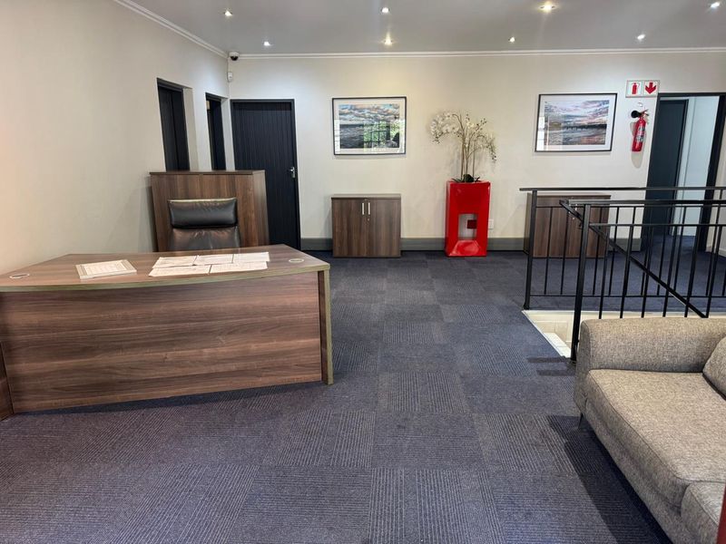 A professional office space featuring carpeted flooring, recessed downlighting, and a metal stair railing leading to a lower level.