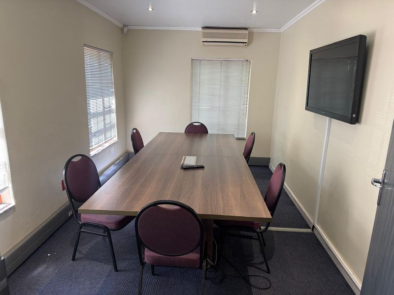 A functional office meeting room featuring carpeted flooring, wall-mounted air conditioning, recessed lighting, and venetian blinds.