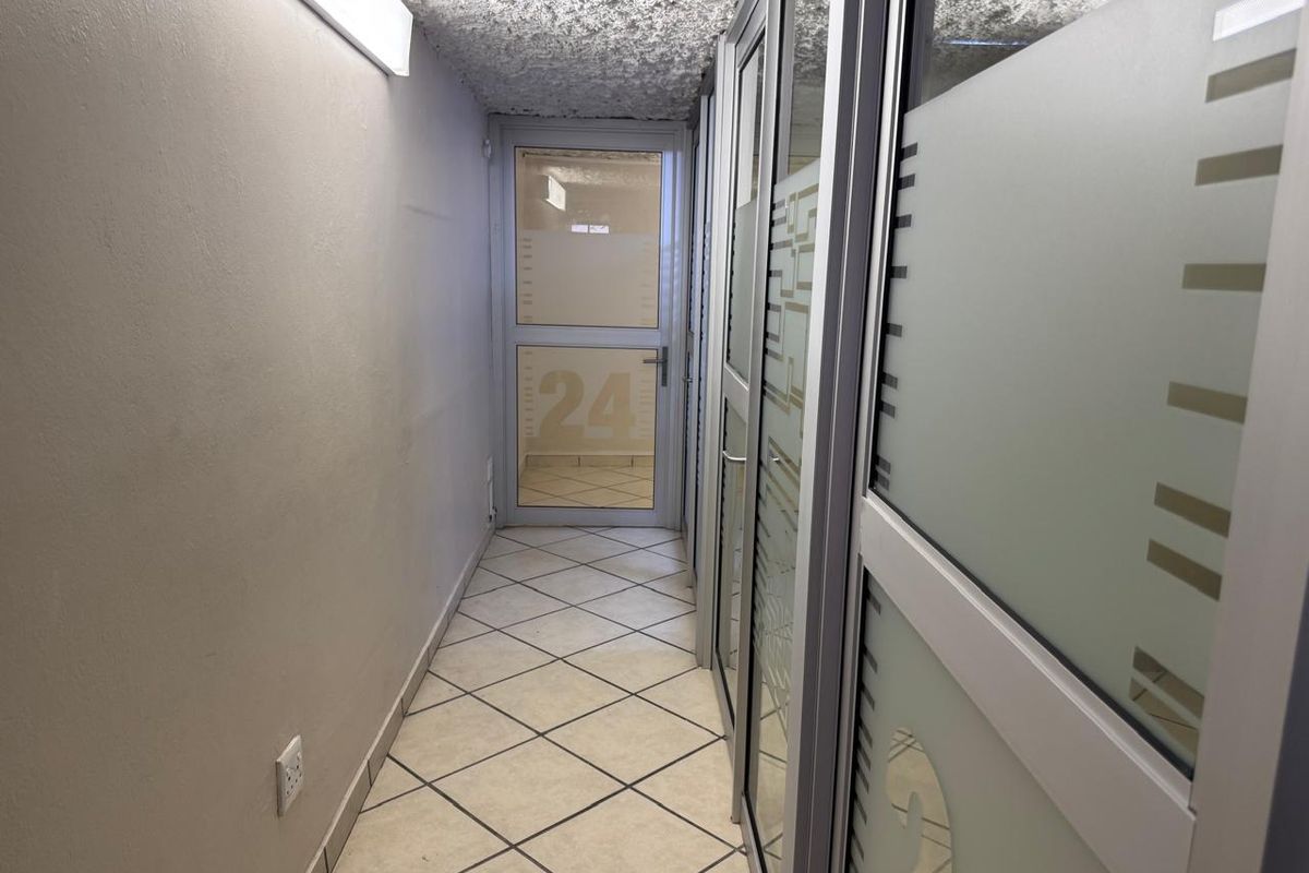A commercial hallway featuring tiled flooring, textured ceilings, and glass partition walls with frosted privacy panels leading to an exterior door.
