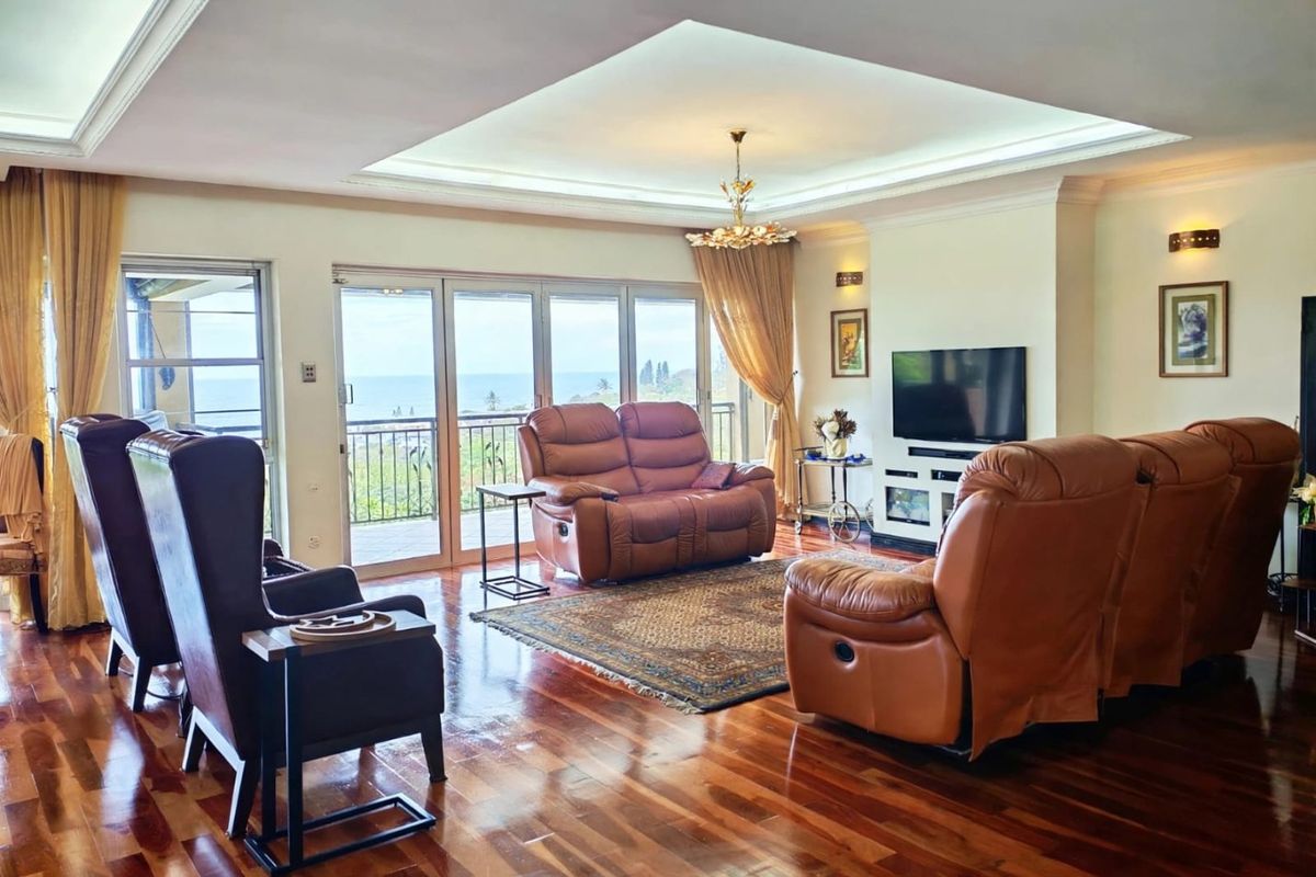 Spacious living room featuring polished hardwood flooring, a recessed tray ceiling with integrated lighting, and large sliding glass doors opening to a balcony with ocean views.