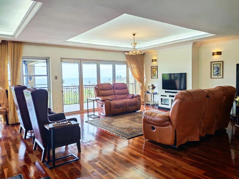 Spacious living room featuring polished hardwood flooring, a recessed tray ceiling with integrated lighting, and large sliding glass doors opening to a balcony with ocean views.