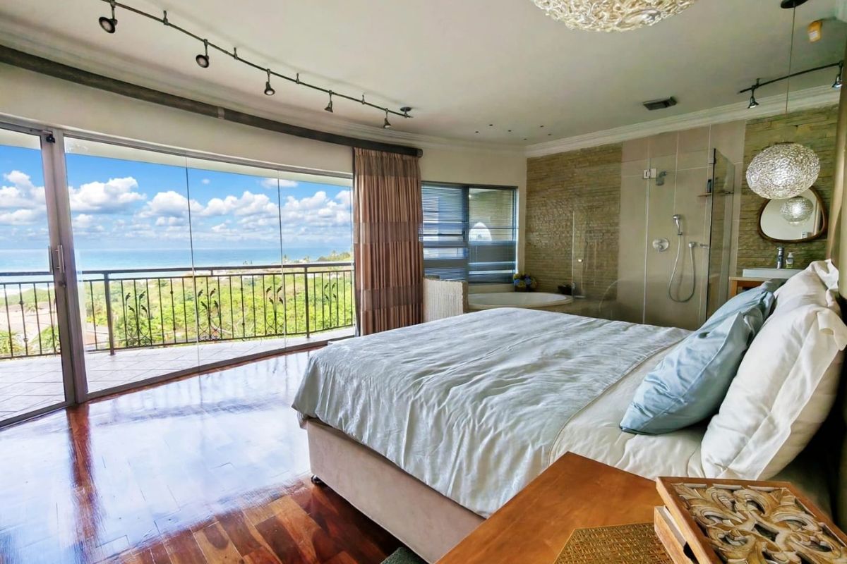 Spacious master bedroom featuring hardwood floors, an open-plan en-suite bathroom with a glass shower and soaking tub, and direct access to a scenic balcony.