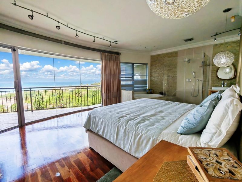 Spacious master bedroom featuring hardwood floors, an open-plan en-suite bathroom with a glass shower and soaking tub, and direct access to a scenic balcony.