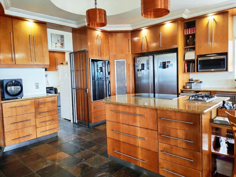 Spacious kitchen featuring warm wood cabinetry, granite countertops, a central island with integrated cooktop, and slate tile flooring with recessed ceiling lighting.