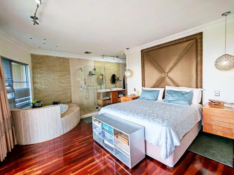 Spacious bedroom featuring an integrated en-suite bathroom with a built-in bathtub, glass shower, double vanity, and elegant stone feature wall.